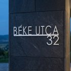 Fehér alumínium házszám tábla utcanévvel, rusztikus téglafal bejáraton feheren