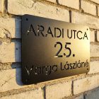 Oldalról megvilágított utcanévtábla, kirajzolódó árnyékkal a falon