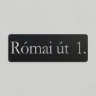 Egy méteres, matt fekete porszórt fém utcatábla fehér vakolatú bejárati falon, lézervágott utcanévvel és házszámmal