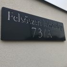 Méteres acél utcatábla modern irodai bejáratnál, ipari loft stílusú térben, téglafalon