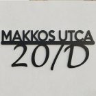 Az L-es lézervágott fém utcatábla teljesen felszerelve, frontális nézet, éles felirattal, valós bejárati falra rögzítve