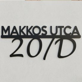 Az L-es lézervágott fém utcatábla teljesen felszerelve, frontális nézet, éles felirattal, valós bejárati falra rögzítve