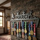 Fekete acél éremtartó oldalról megvilágítva, éles árnyék fehér falon