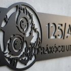Fekete alumínium utcatábla bagoly motívummal, kerti lámpa fényében – esti utcakép